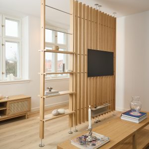 WoodUpp Raumteiler mit vertikalen Eichenlamellen, freistehender Trennwandkonstruktion und schlanken Metallstützen; auf der Rückseite integrierte, offene Holzregalböden und eine dezente Ablage unter dem wandmontierten Fernseher. Die schmalen Lamellen mit gleichmäßigen Zwischenräumen erzeugen Blickschutz, während höhenverstellbare Regalbretter Stauraum bieten; ideal als Raumteiler und Medienwand.