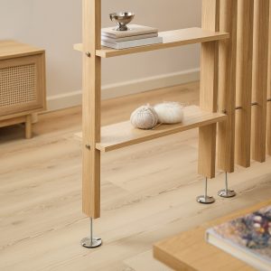 WoodUpp Raumteiler aus hellem Eichenholz mit feiner sichtbarer Holzmaserung und minimalistischem, skandinavisch inspiriertem Design, schlanken vertikalen Lamellen, zwei aufgesetzten Regalböden und verstellbaren Metall-Fußplatten. Auf den Böden liegen zwei Knäuel Wolle, Stricknadel, ein Stapel Bücher und eine kleine silberne Schale als Dekoration.