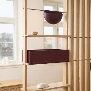 WoodUpp Regalraumteiler aus hellem Eichenholz mit schlanken Stäben und sichtbaren Metallstangen, bestückt mit einer breiten weinroten Filzbox und einer passenden hängenden halbkugelförmigen Pflanzschale. Auf den Regalböden liegen eine kleine handgedrehte Holzschale und ein heller dekorativer Stein im eleganten nordischen Stil.