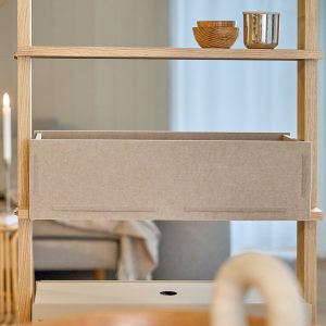 WoodUpp Regal aus hellem Eichenholz in offener Leiterkonstruktion, bestückt mit einer beigen WoodUpp Filzbox als Schublade. Auf dem oberen Brett zwei kleine Holzschalen und ein glänzender Metallbecher. Die feine Holzmaserung ist sichtbar, die Filzbox wirkt weich und funktional und schafft eine ruhige, wohnliche Atmosphäre.