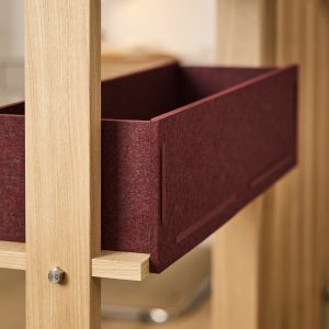 Nahaufnahme eines WoodUpp-Regals aus hellem Eichenholz: sichtbare Holzstreben mit Metallverbindungsschraube und eine herausgezogene, bordeauxrote Filzschublade/Box, die auf schmalen Holzauflagen ruht. Die Filzoberfläche wirkt strukturiert und stabil, das Eichenholz feinporig und naturbelassen. Design minimalistisch und handwerklich präzise, wohnlicher Akzent für Zuhause und funktional.