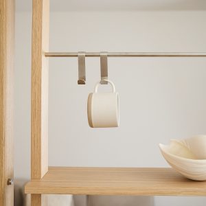 WoodUpp-Regal aus hellem Eichenholz mit sichtbarer Maserung, kombiniert mit schlanker, gebürsteter Edelstahlstange und zwei geschwungenen WoodUpp-Haken, an denen eine matte, hellbeige Keramiktasse hängt. Auf dem Regalbrett steht eine organisch geformte, cremefarbene Schale als dekoratives Detail. Die reduzierte, skandinavisch inspirierte Komposition betont neutrale Farbtöne und funktionales Design.