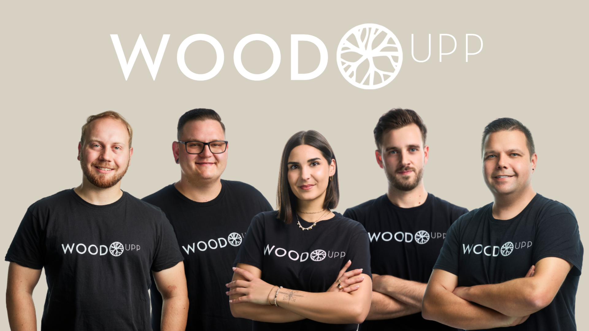 Ein Gruppenfoto des WoodUpp Teams, bestehend aus fünf Personen – vier Männern und einer Frau in der Mitte mit verschränkten Armen. Sie stehen vor einem beigen Hintergrund unter einem großen, weißen WoodUpp-Logo. Alle tragen schwarze T-Shirts, die deutlich mit dem WoodUpp-Logo und Markennamen auf der Brust bedruckt sind.